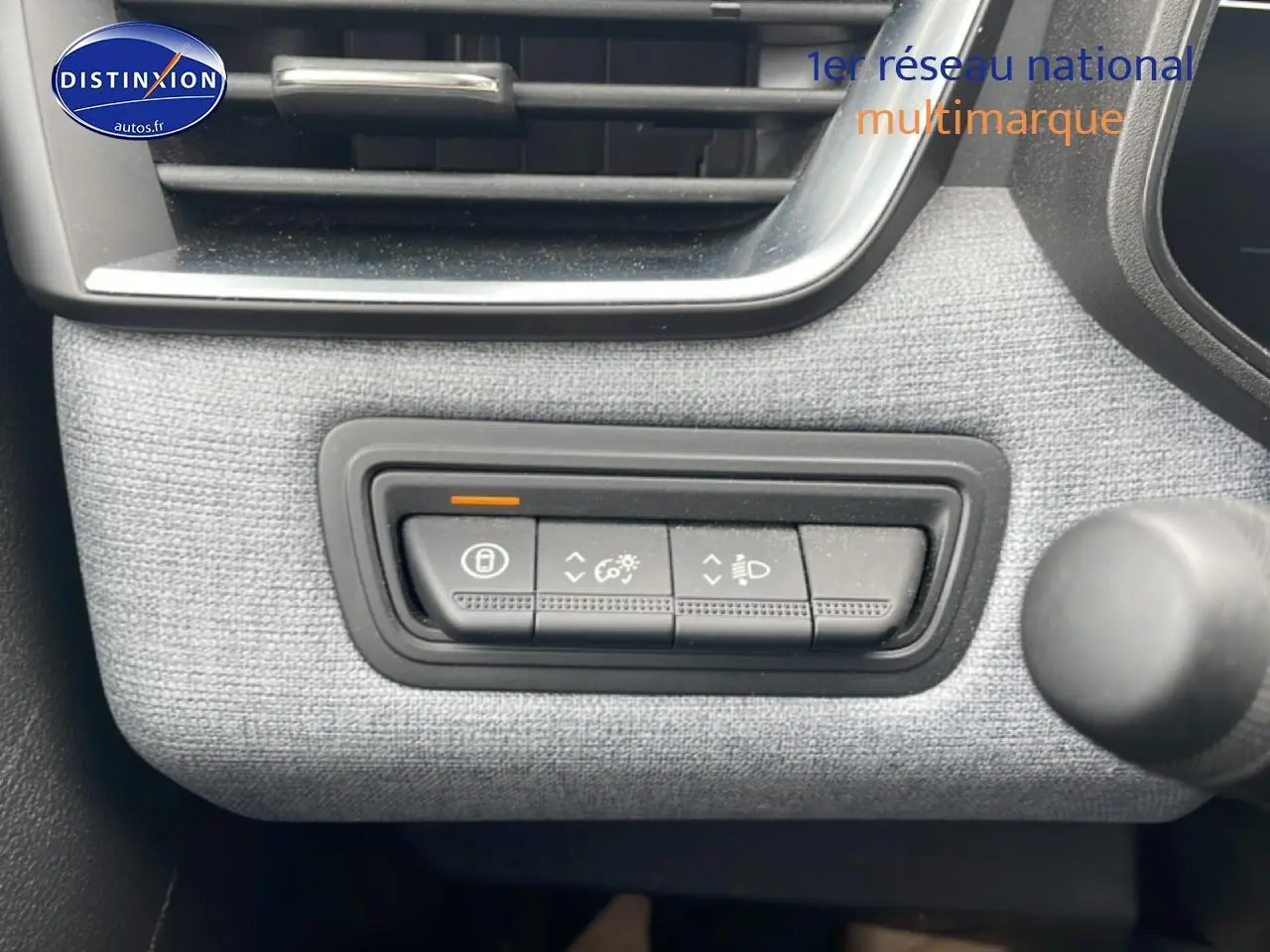 Gros plan sur les commandes de réglage d’éclairage et verrouillage dans l’habitacle gris clair de la Renault Clio V blanche.