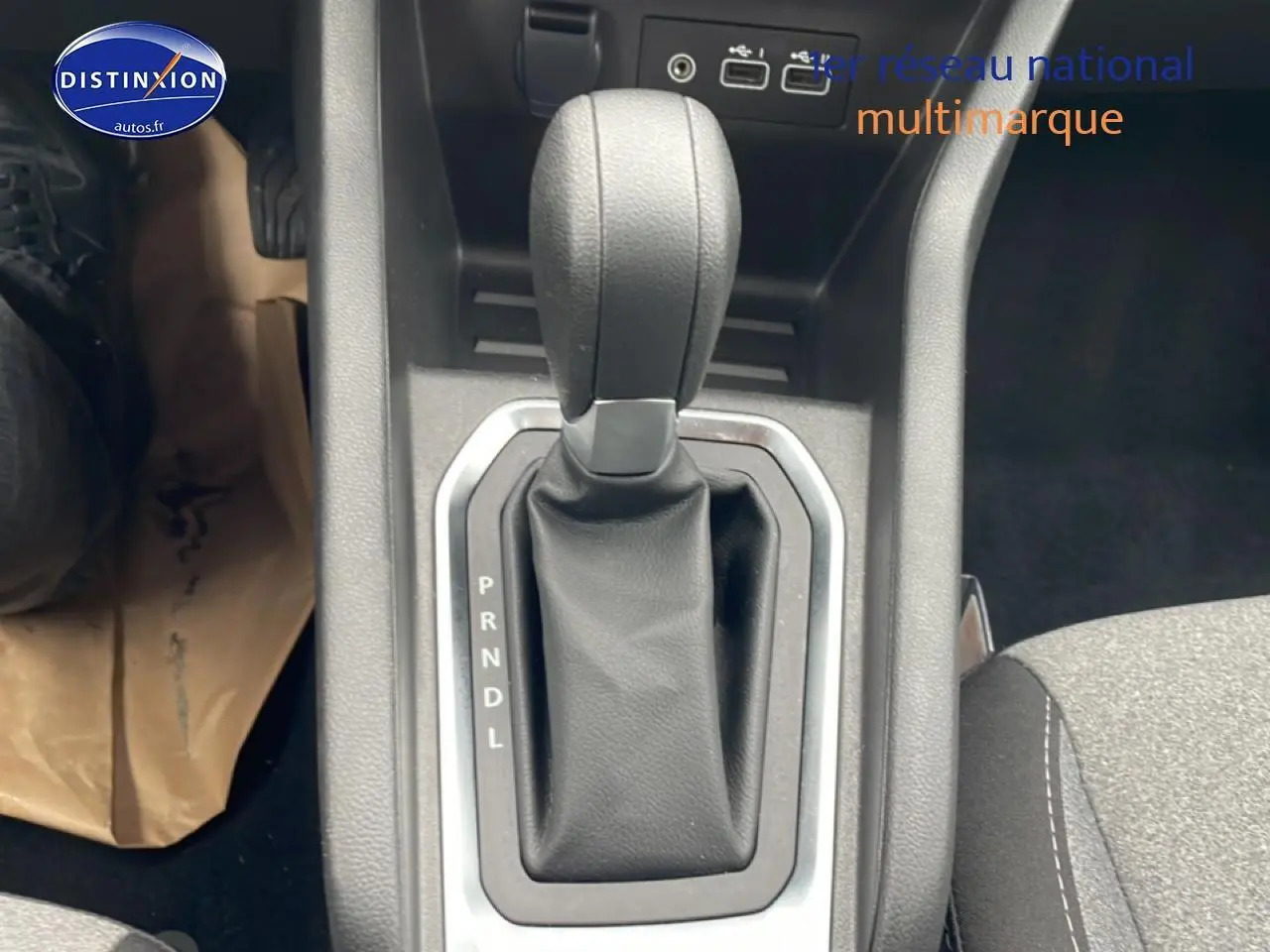 Le levier de vitesse automatique noir de la Renault Clio V 2025 vu de dessus avec console grise et siège tissu gris.