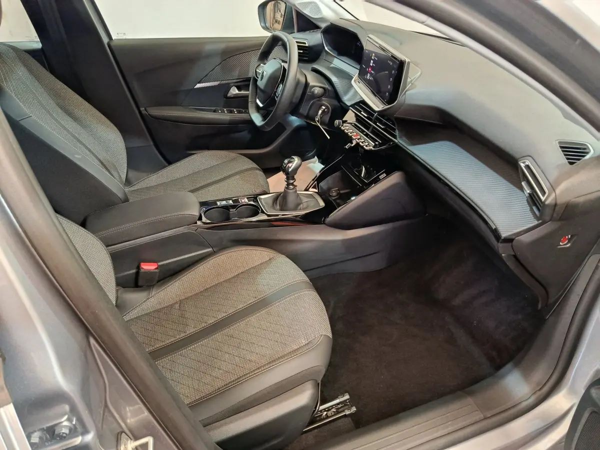 Vue intérieure côté conducteur de la Peugeot 208 PureTech 100 S&S Allure 2025, montrant sièges gris et écran tactile central.