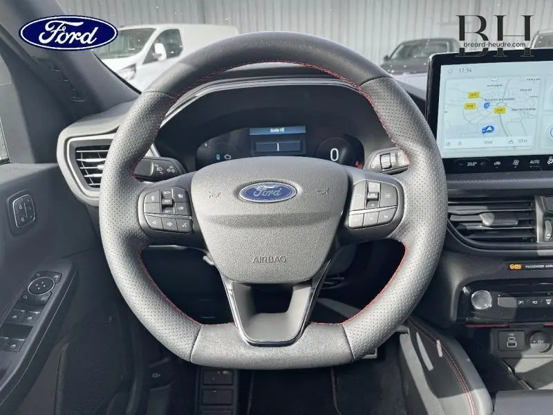 Vue intérieure centrée sur le volant sport noir avec surpiqûres rouges du Ford Kuga gris Solar Métallisée, tableau de bord et écran tactile visibles.