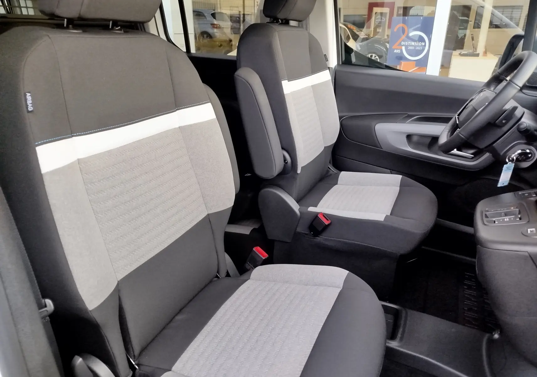 Vue intérieure côté conducteur du Citroën Berlingo 2025, sièges tissu gris clair et noir avec détails blancs.
