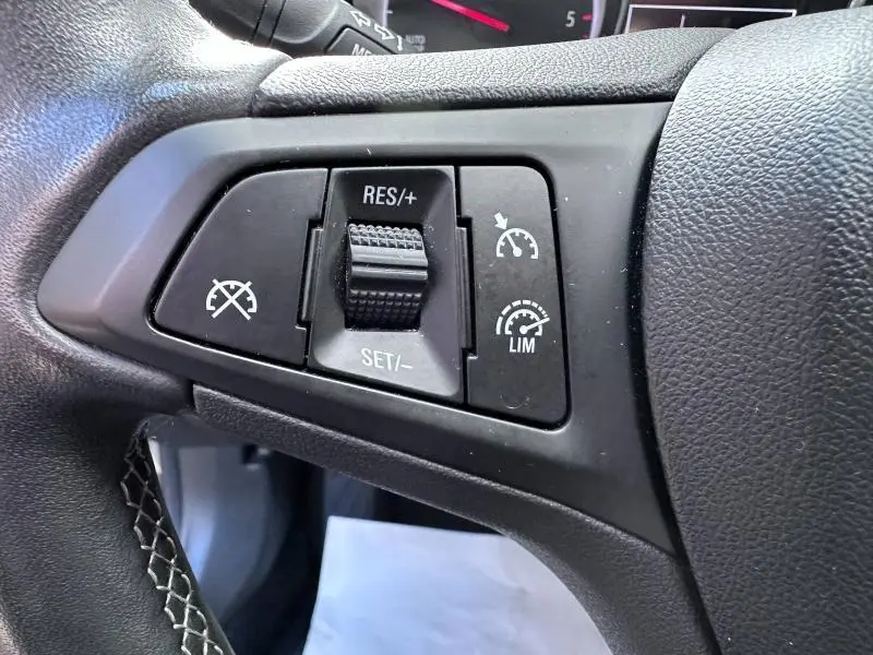 Gros plan sur les commandes de régulateur de vitesse sur le volant noir de l'Opel Astra Sports Tourer gris cosmique.