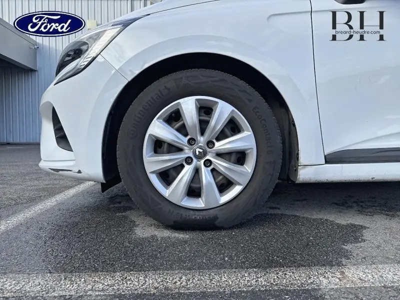 Gros plan sur la roue avant gauche d'une Renault Clio blanche 2020 avec enjoliveur et logo Renault visible.