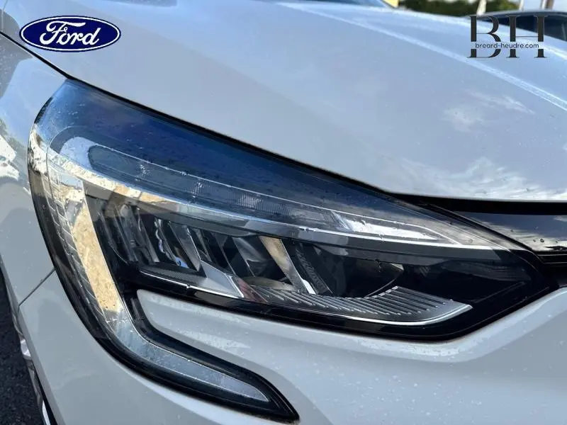 Gros plan sur le phare avant droit de la Renault Clio blanche, soulignant ses lignes modernes et son éclairage LED.