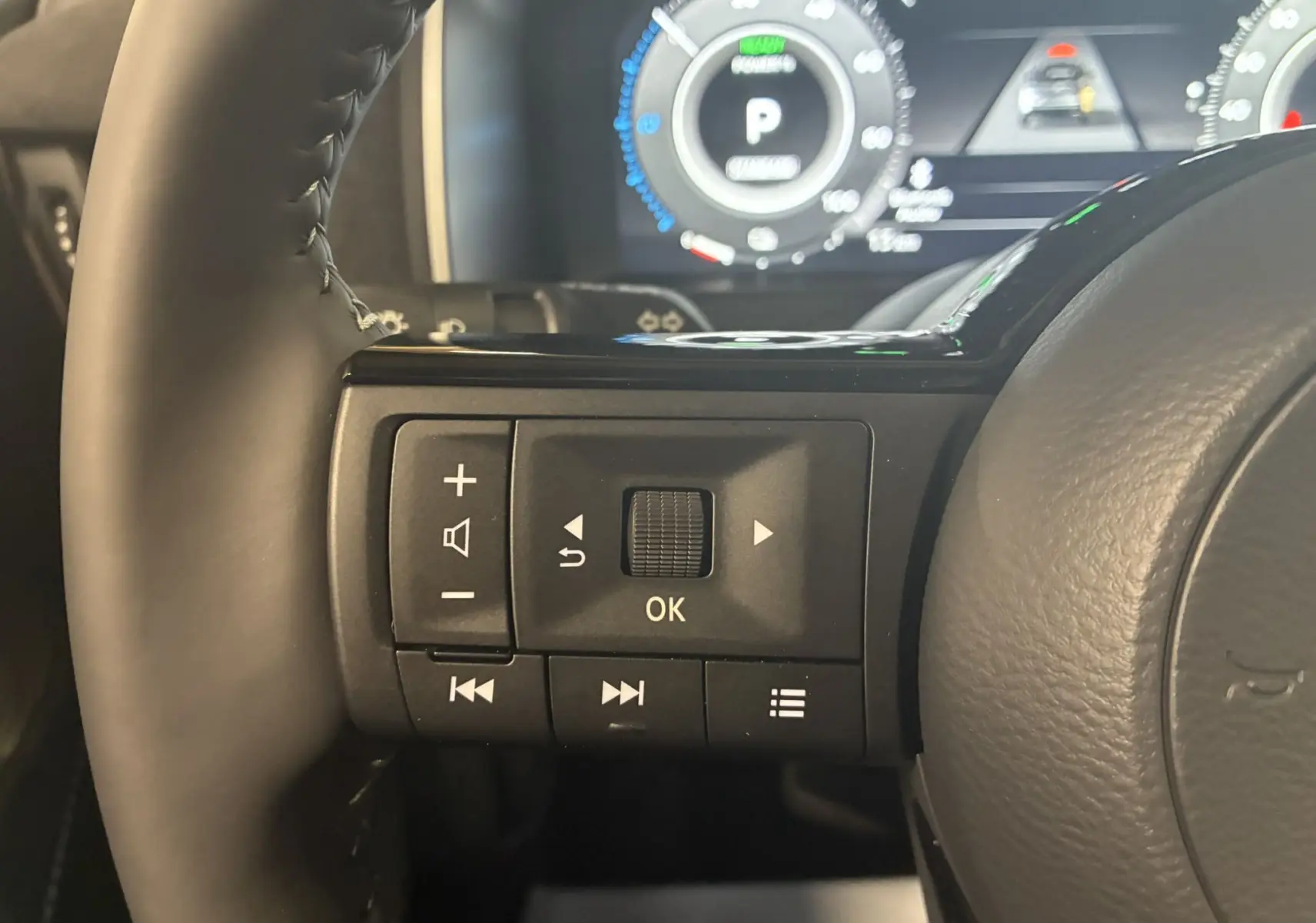 Gros plan sur les commandes gauche du volant noir du Nissan Qashqai 2025 avec tableau de bord numérique en arrière-plan.