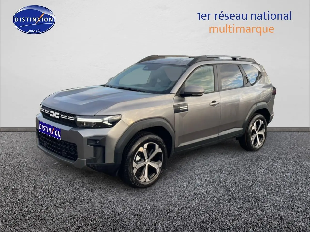 SUV Dacia Bigster gris schiste en 3/4 avant droit, avec jantes alliage diamantées et barres de toit visibles.