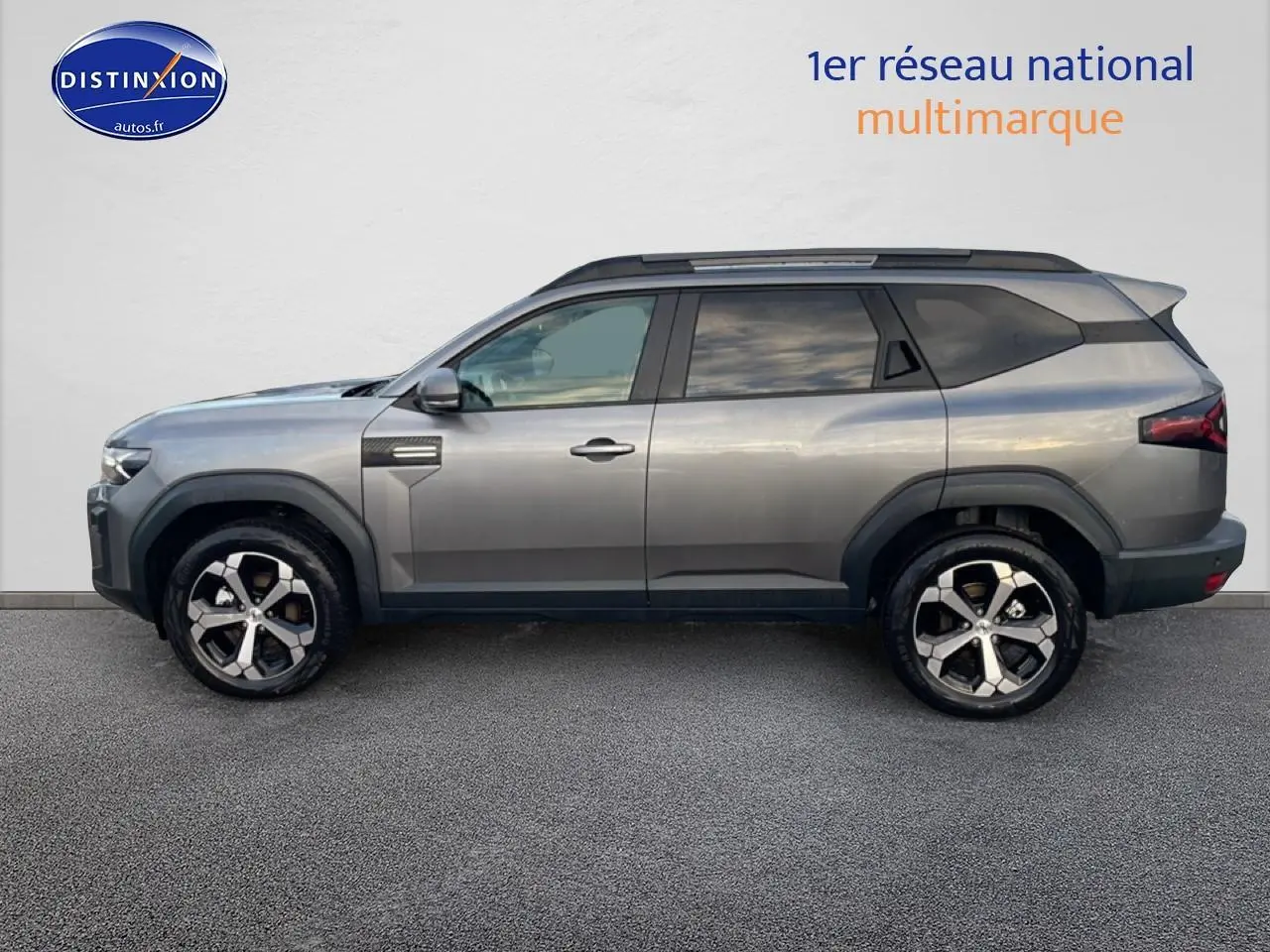 Vue de profil côté gauche du SUV Dacia Bigster gris schiste avec jantes alliage diamantées et barres de toit noires.