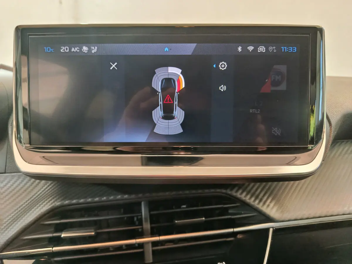 Écran tactile central de la Peugeot 208 gris foncé affichant l'aide au stationnement avec alertes visuelles.