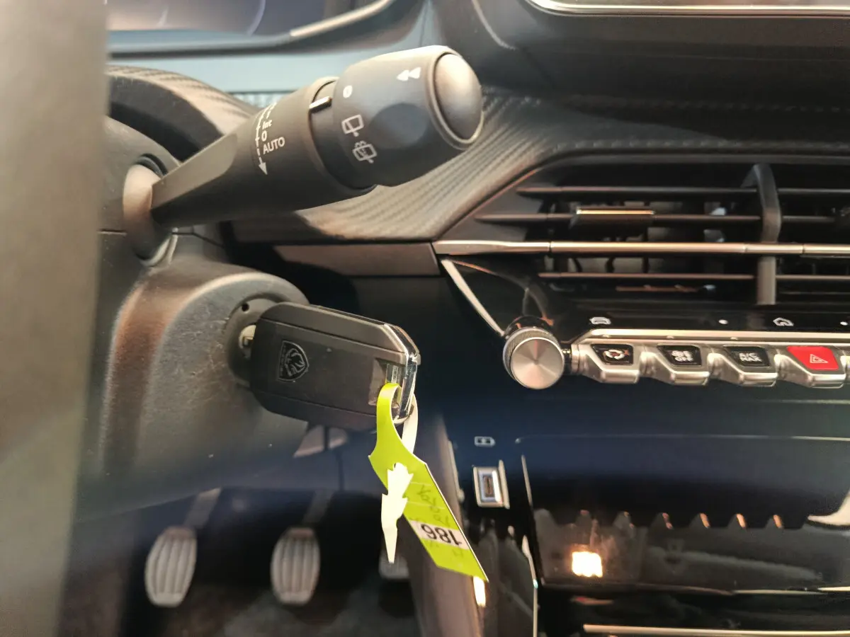 Gros plan intérieur côté conducteur du tableau de bord noir et de la clé insérée dans une Peugeot 208 gris foncé 2025.