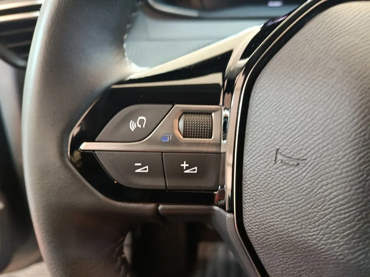 Gros plan sur les commandes gauche du volant noir du Peugeot 208 2025, boutons de volume et téléphone visibles.