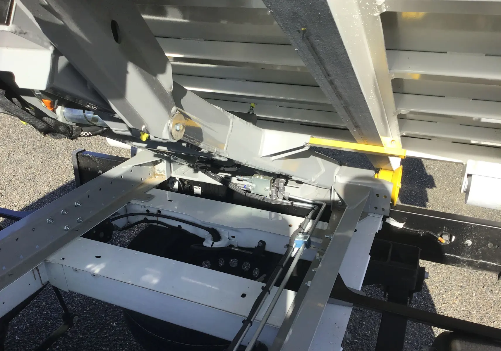 Vue en gros plan sous la benne du Ford Transit Chassis Cabine blanc, montrant le bras de levage et le châssis métallique.