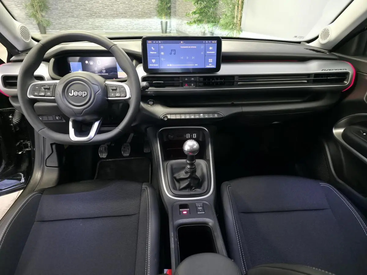 Vue intérieure avant du Jeep Avenger noir 2025, tableau de bord moderne avec écran tactile et levier de vitesses manuel.