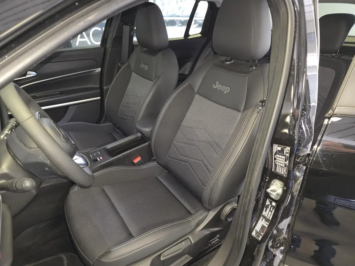 Vue intérieure côté conducteur du Jeep Avenger noir 2025, sièges tissu/TEP noirs avec logo Jeep brodé.