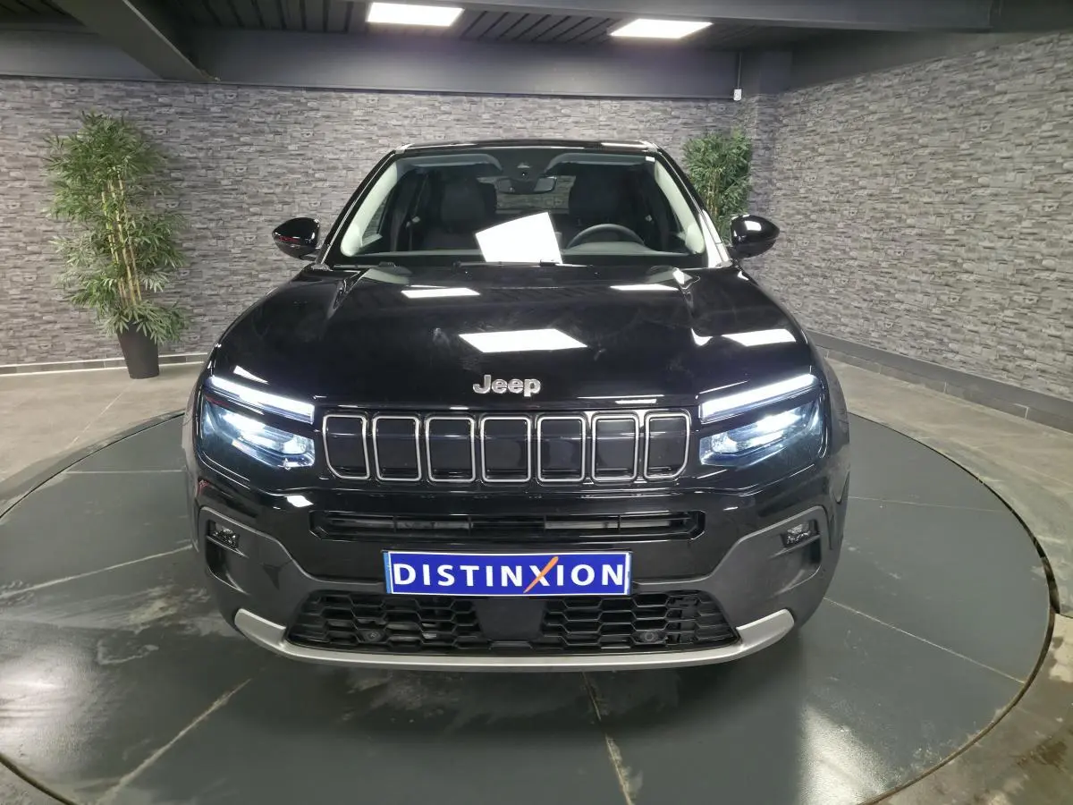 Vue avant d'un Jeep Avenger noir 2025 avec calandre gloss black et phares LED allumés en intérieur showroom.