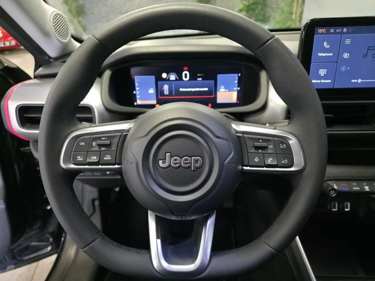 Vue rapprochée du volant noir Jeep Avenger 2025 avec commandes intégrées et tableau de bord numérique en arrière-plan.