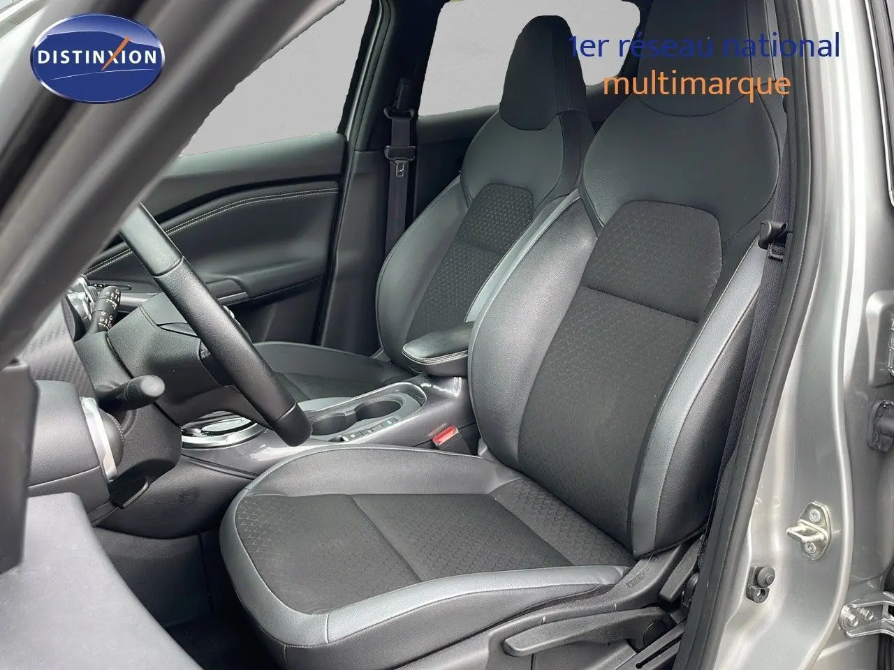 Intérieur avant droit du Nissan Juke Hybrid 2023 gris perle métal, sièges en tissu et cuir noir avec console centrale visible.