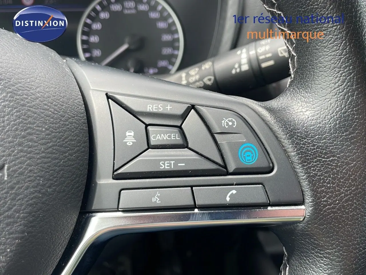 Gros plan sur les commandes au volant d'un Nissan Juke Hybrid 2023 gris perle, avec régulateur de vitesse et fonctions vocales.