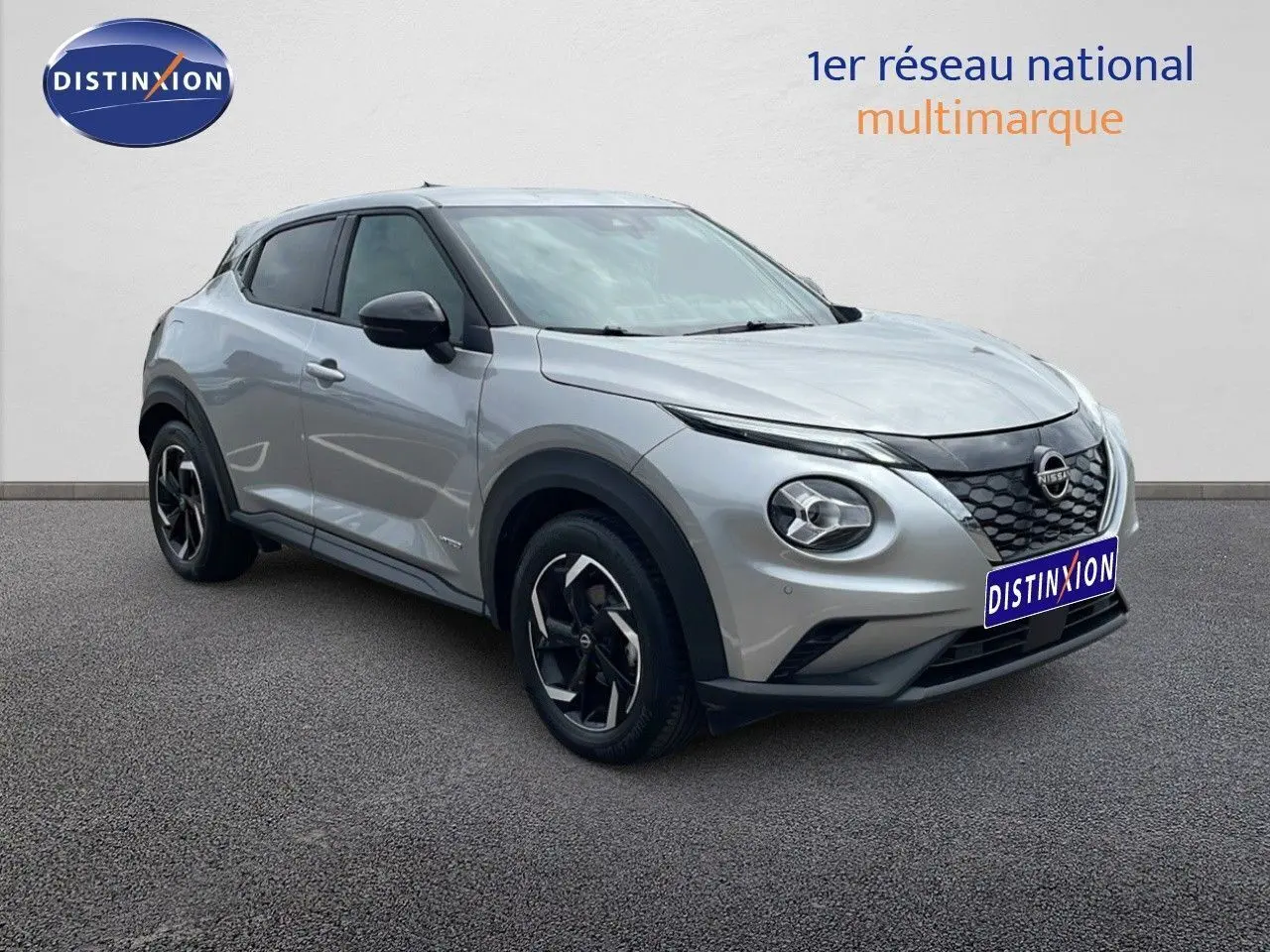 Nissan Juke Hybrid gris perle métal vu en 3/4 avant droit, avec jantes noires et calandre distinctive.