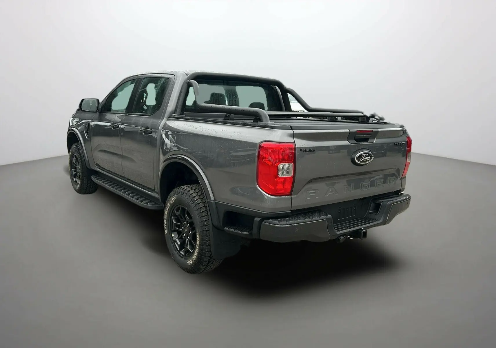 Ford Ranger 2025 gris carbone en vue 3/4 arrière droit, avec benne et barres de protection noires visibles.