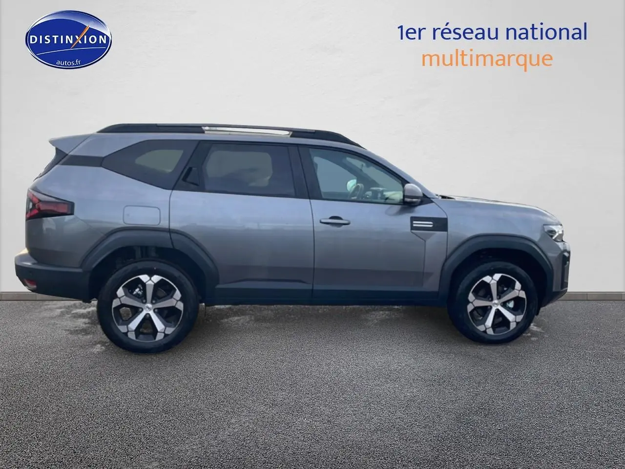 Vue de profil droit du Dacia Bigster gris schiste 2025 avec jantes alliage 18 pouces et barres de toit noires.