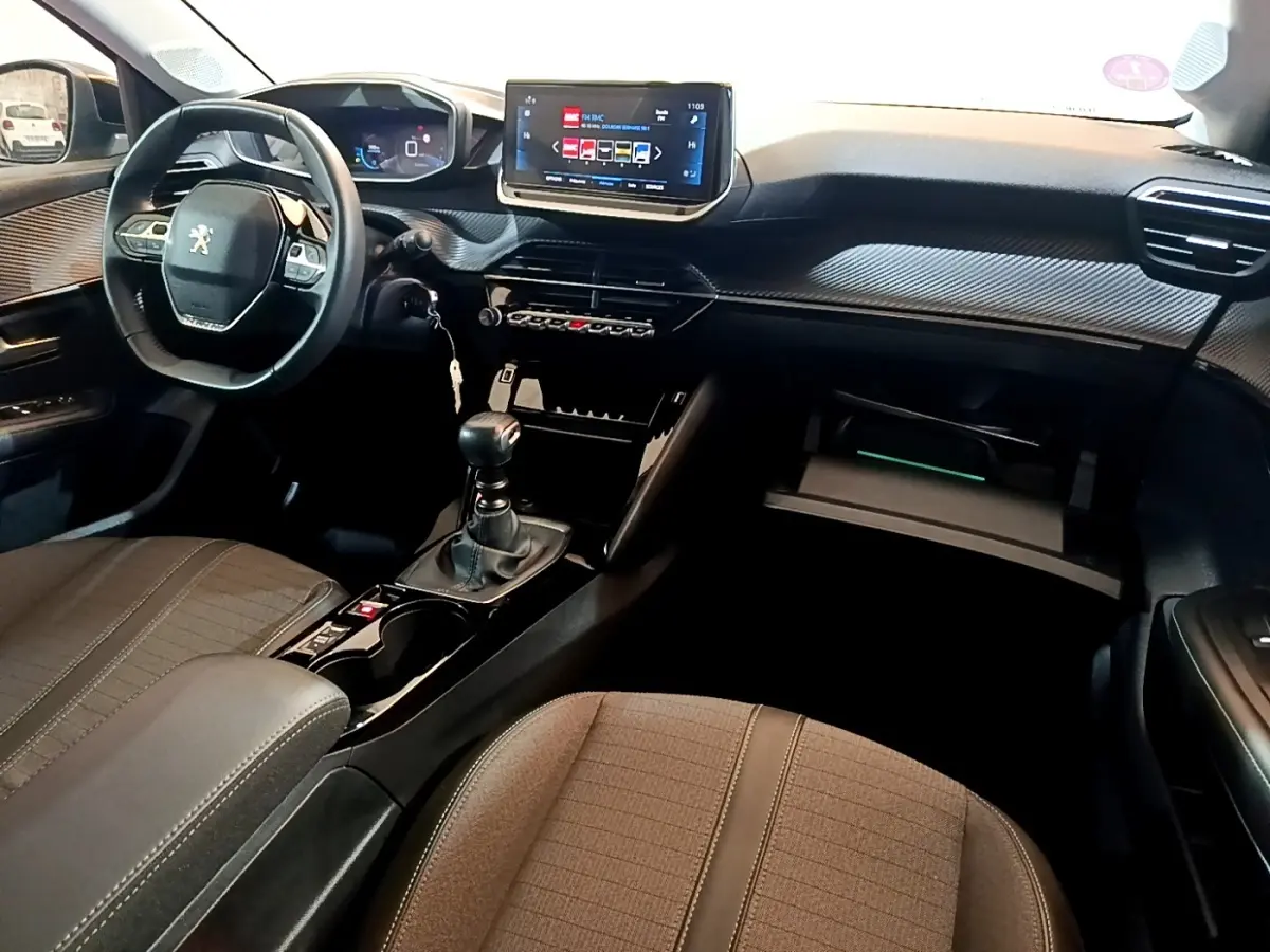 Intérieur avant de la Peugeot 208 PureTech 100 S&S Allure Pack 2023, vue côté conducteur avec tableau de bord numérique et volant cuir.