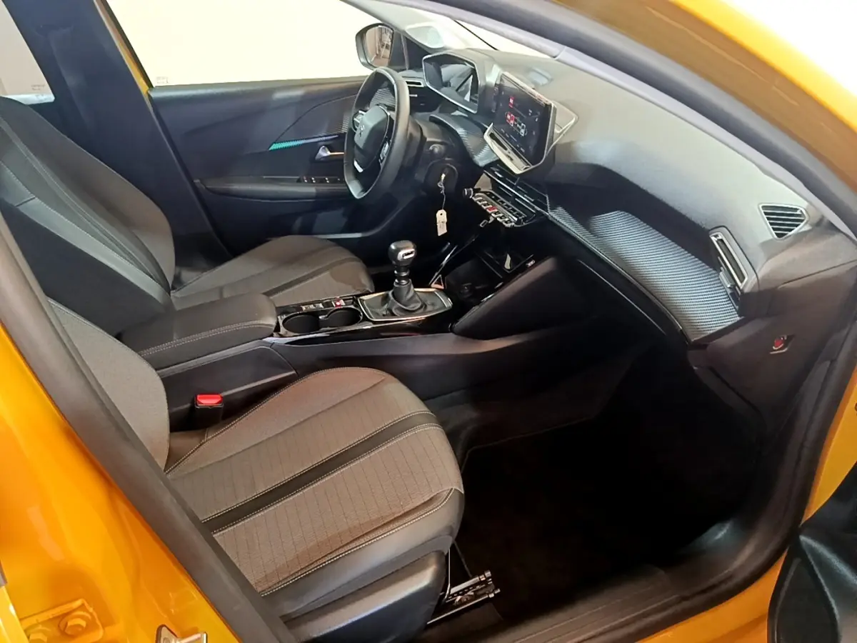Vue intérieure côté conducteur d'une Peugeot 208 jaune 2023, volant cuir multifonctions et écran tactile central visible.