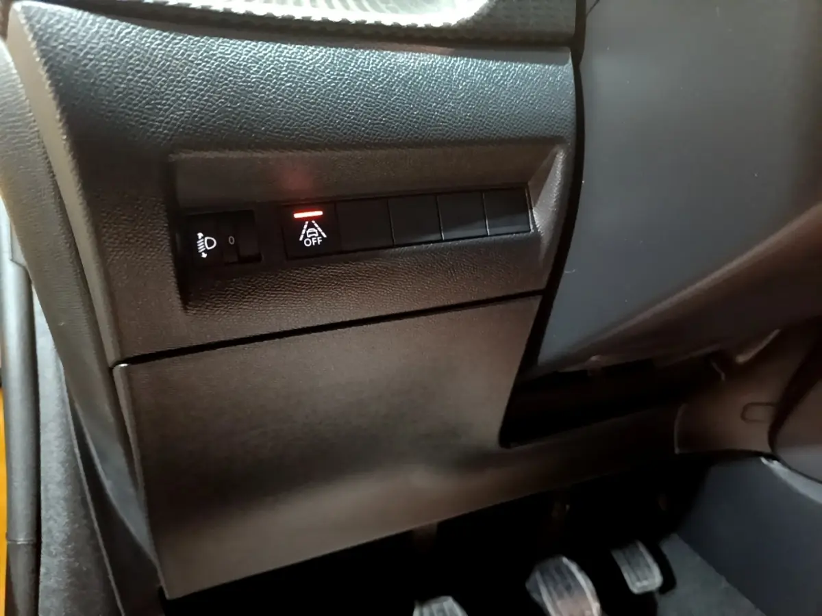 Détail du tableau de bord côté gauche de la Peugeot 208 jaune, avec commandes d'éclairage et assistance désactivée.