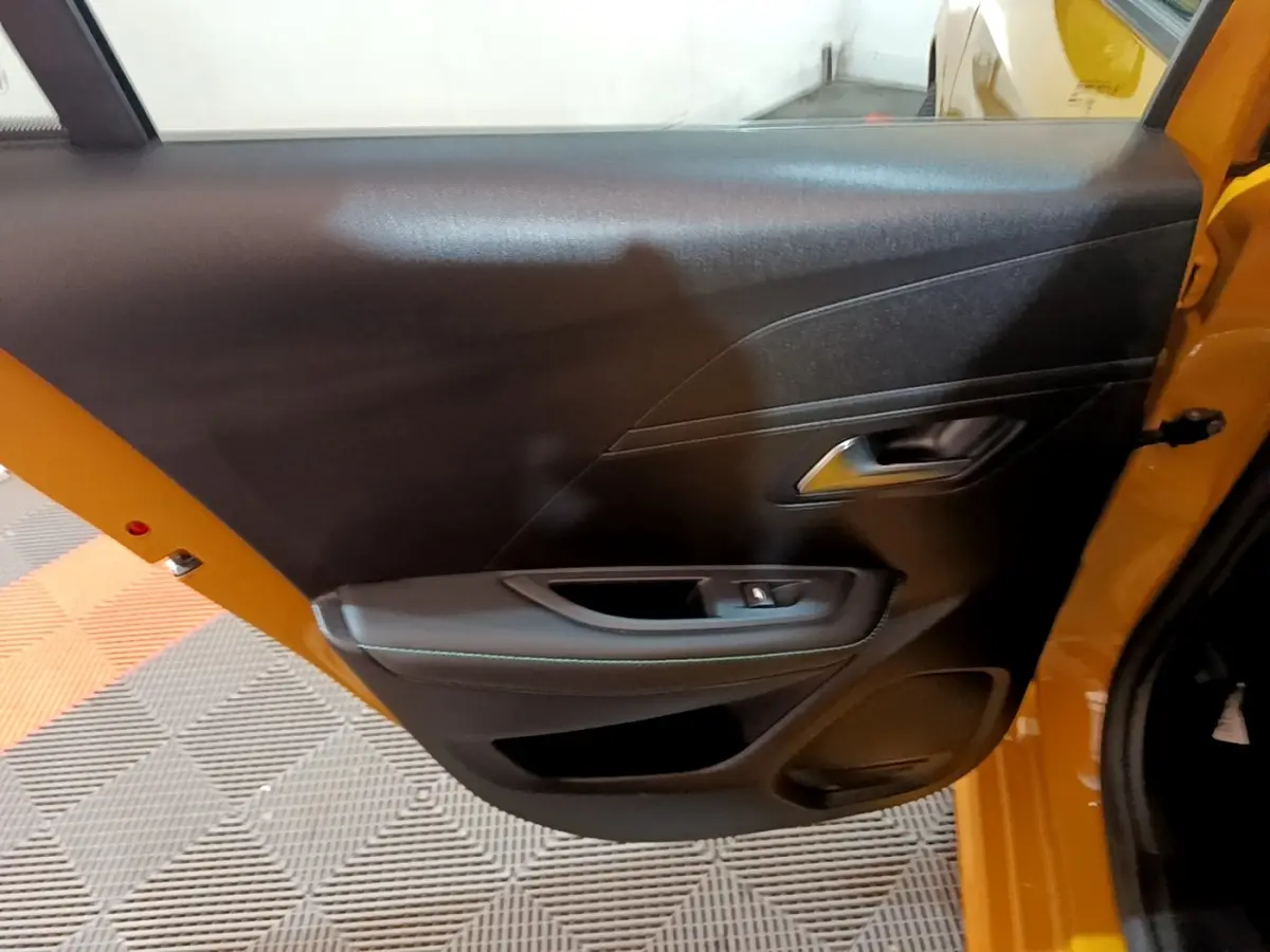 Vue intérieure de la porte arrière droite noire sur Peugeot 208 jaune, avec poignée et commande de vitre visible.