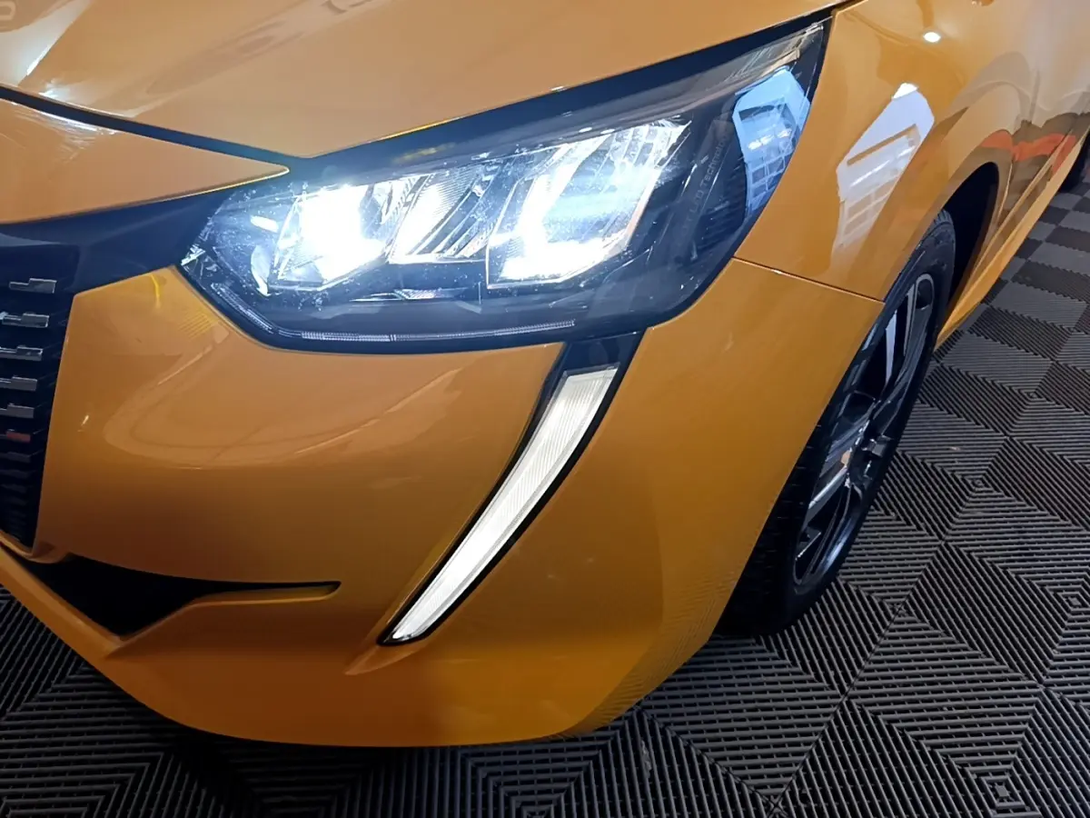 Gros plan sur l'avant droit jaune vif de la Peugeot 208 2023 avec phares LED allumés et jante noire.