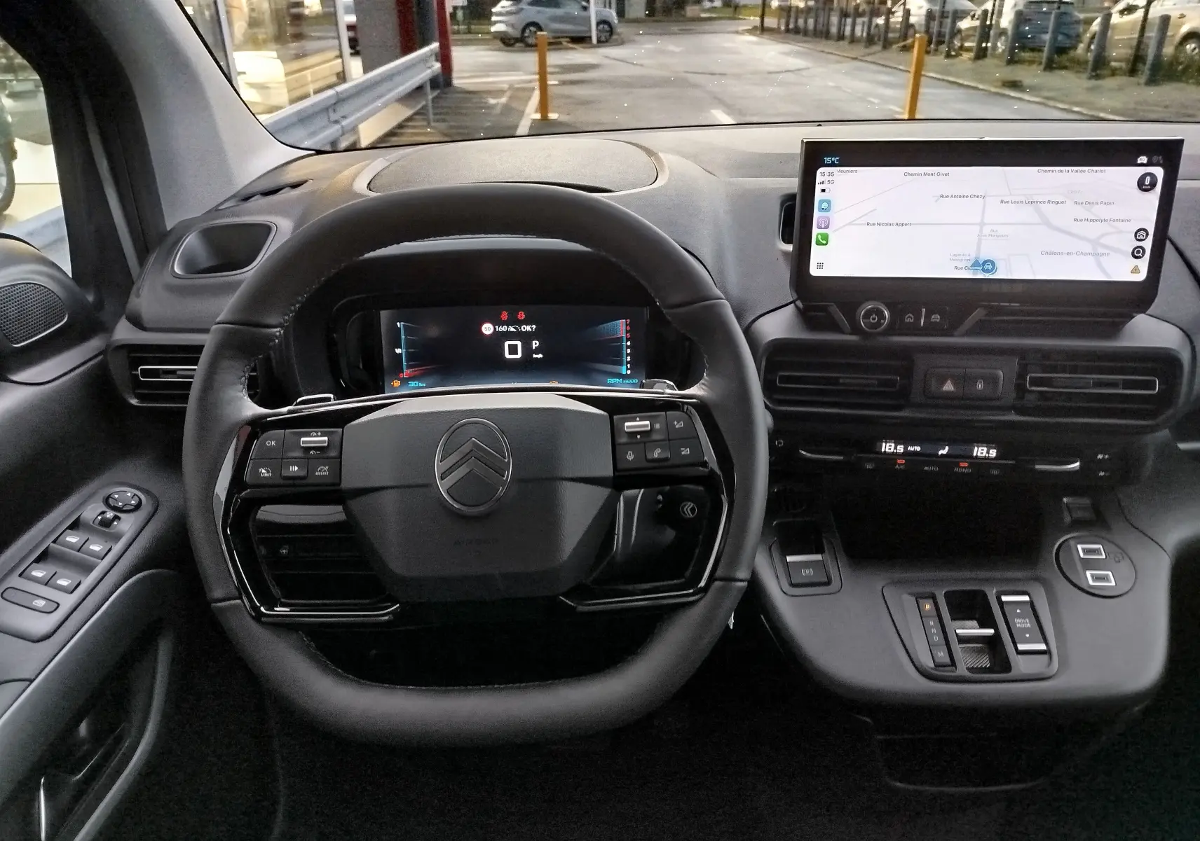 Vue intérieure centrée sur le volant et le tableau de bord numérique du Citroën Berlingo gris acier avec écran tactile de navigation.