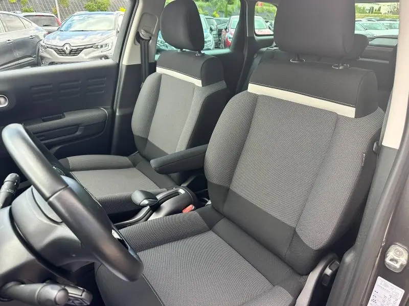 Intérieur avant du Citroën C3 Aircross 2021, sièges tissu Mica Grey gris avec accoudoir côté droit, volant cuir noir visible.