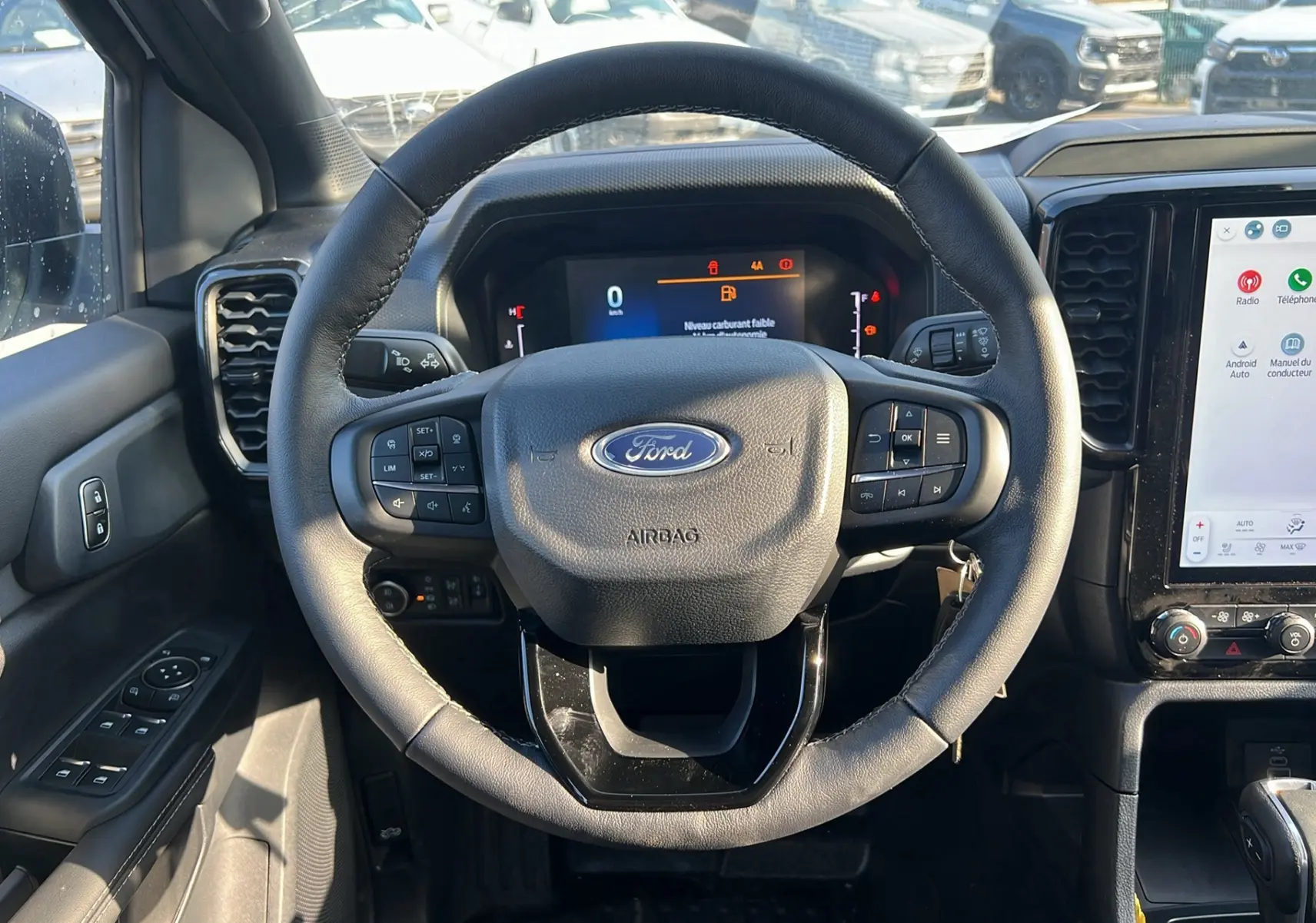 Vue intérieure centrée sur le volant du Ford Ranger 2025 blanc glacier, avec tableau de bord numérique et écran tactile visible.