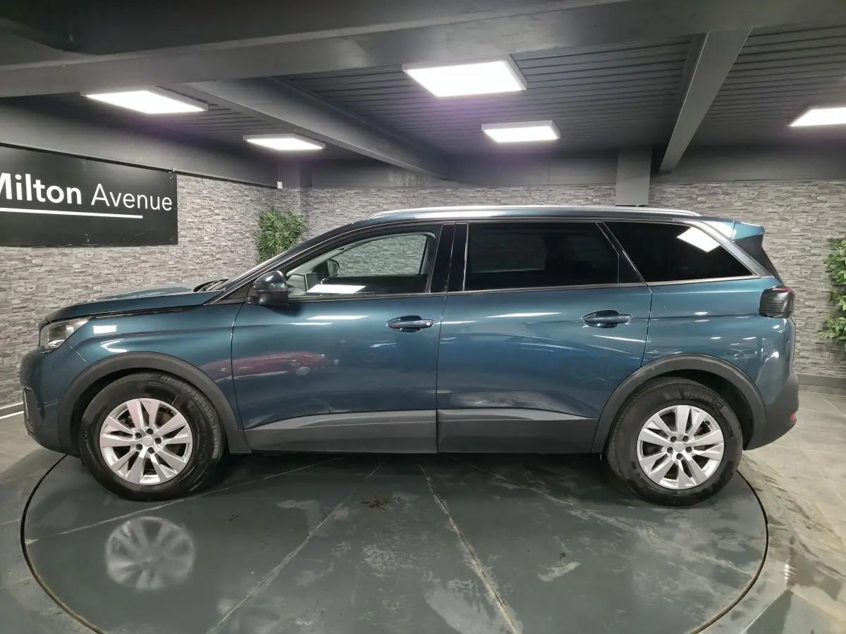 Profil côté gauche du Peugeot 5008 bleu métallisé 2019 avec jantes alliage et vitres surteintées en intérieur showroom.