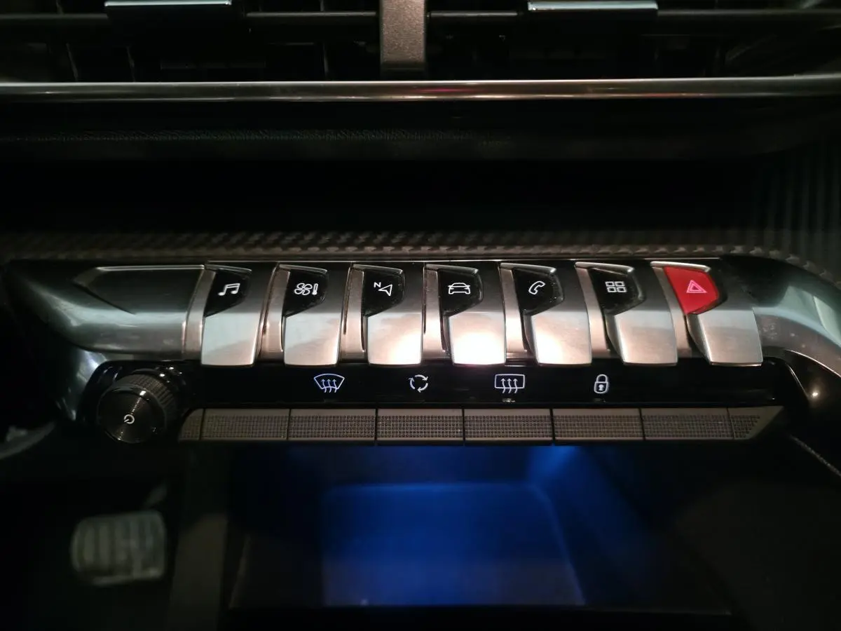 Gros plan sur la rangée de boutons chromés du tableau de bord du Peugeot 5008 bleu, avec éclairage bleu en dessous.
