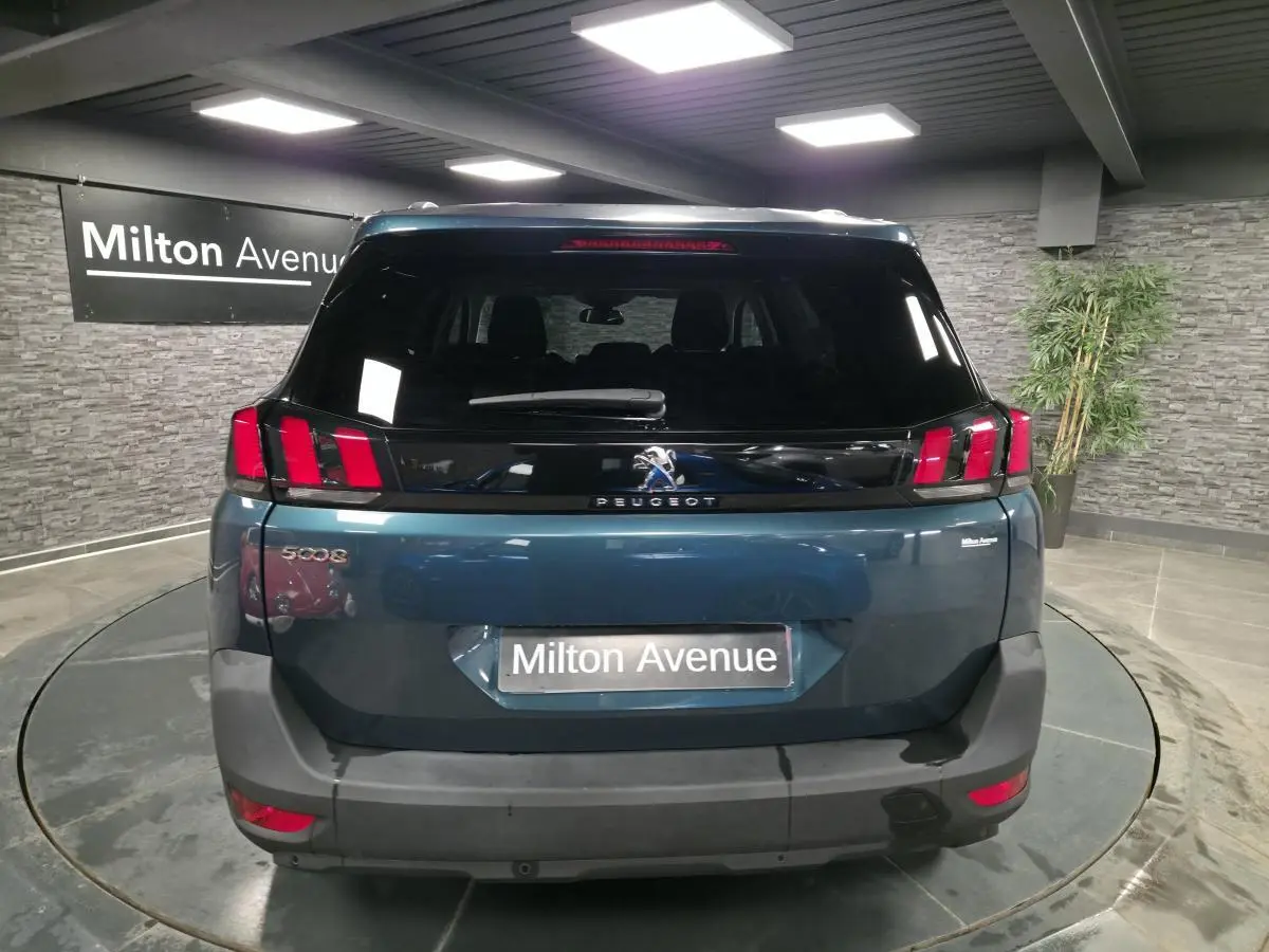 Vue arrière d'un Peugeot 5008 bleu métallisé avec feux arrière à griffes rouges dans un showroom.