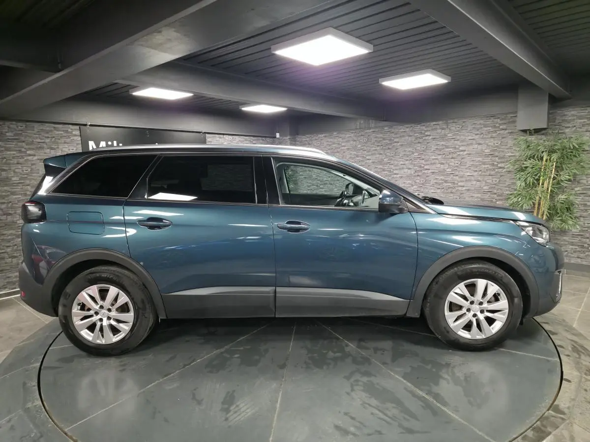 Profil droit d'un Peugeot 5008 bleu métallisé avec jantes alliage 17 pouces dans un showroom intérieur.