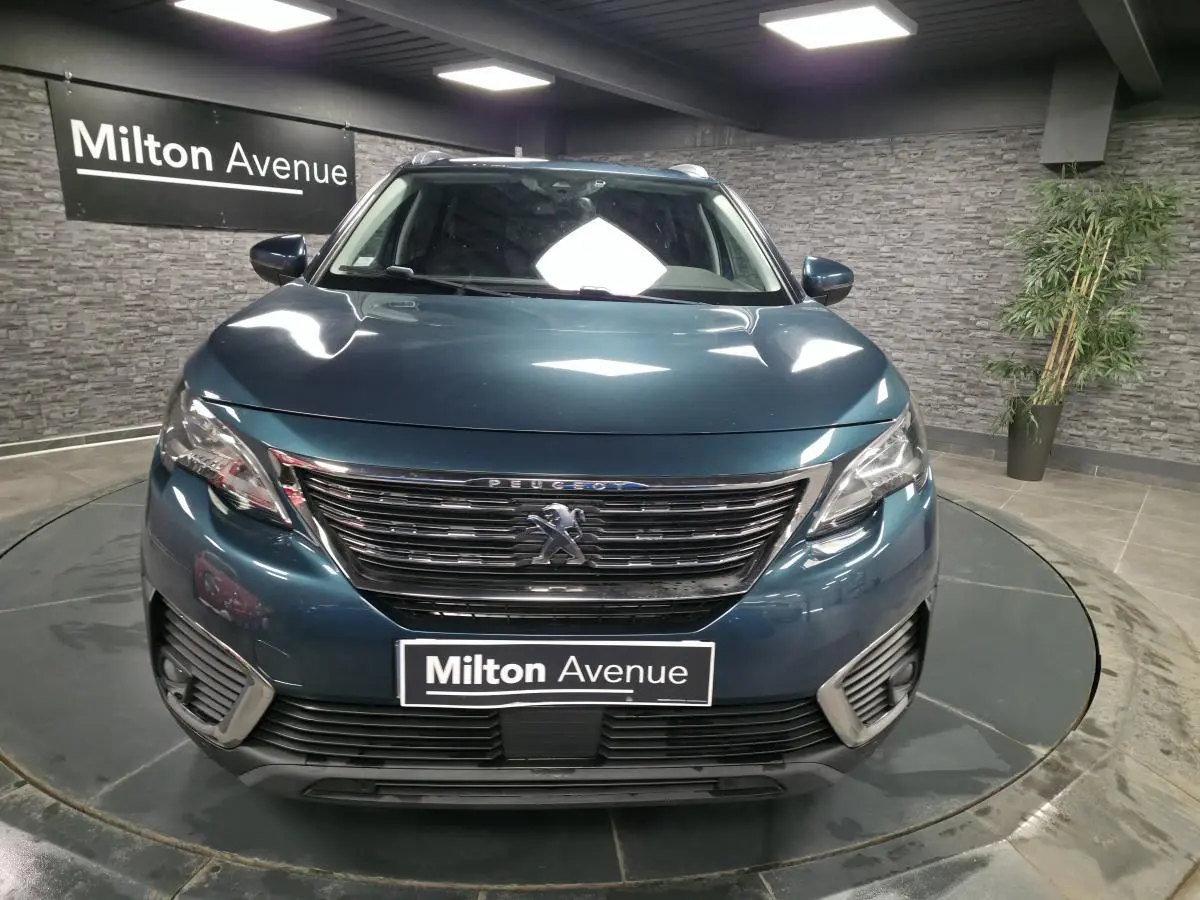 Vue frontale d'un Peugeot 5008 bleu métallisé avec calandre chromée et phares halogènes dans un showroom.