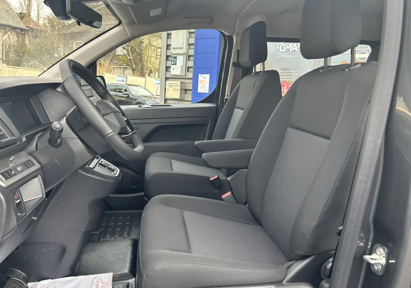 Vue intérieure côté conducteur du Citroën Jumpy cabine approfondie 2025, sièges tissu noir et console centrale visible.