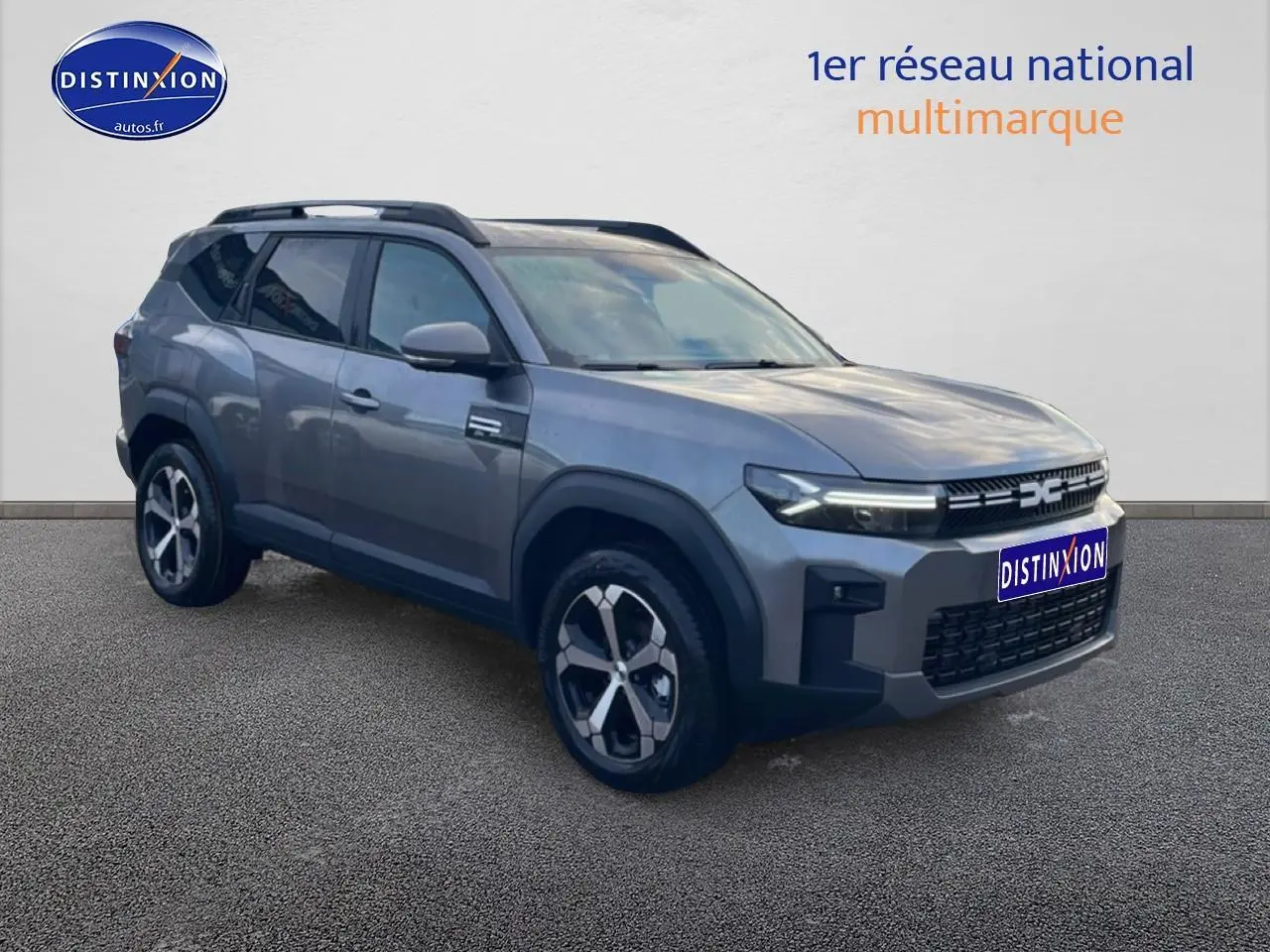 SUV Dacia Bigster gris schiste en 3/4 avant droit, avec jantes alliage diamantées et barres de toit noires.