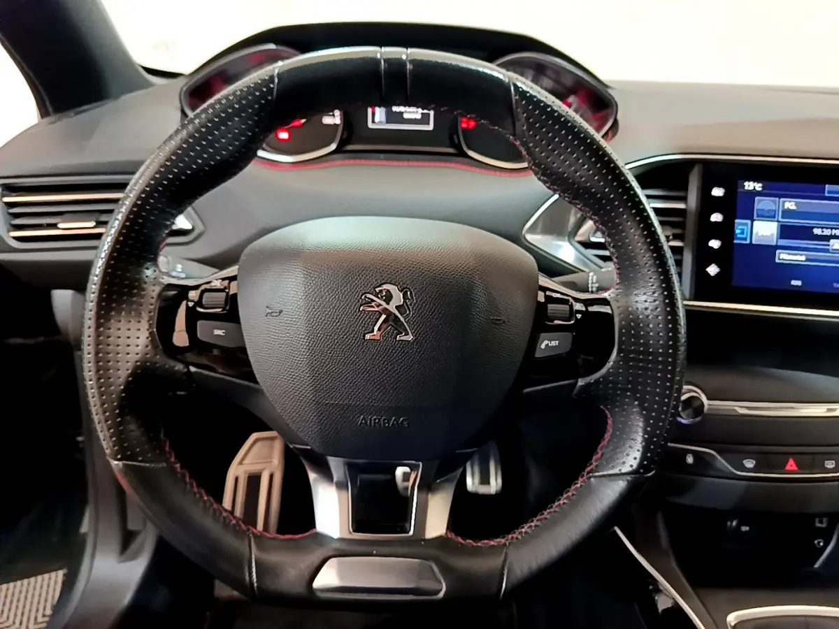 Vue rapprochée du volant cuir perforé noir avec surpiqûres rouges de la Peugeot 308 GT Line 2016, tableau de bord et écran tactile visibles.