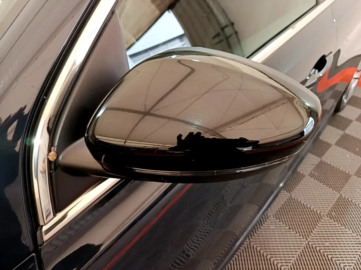Gros plan sur le rétroviseur droit noir brillant d'une Peugeot 308 gris foncé, reflet de l'environnement intérieur visible.