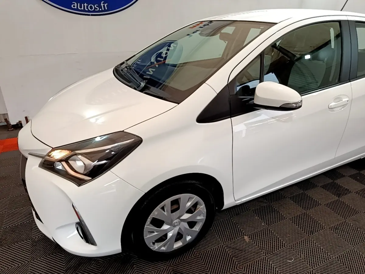 Vue 3/4 avant droit d'une Toyota Yaris blanche 2019 avec phares allumés et jantes alliage visibles.