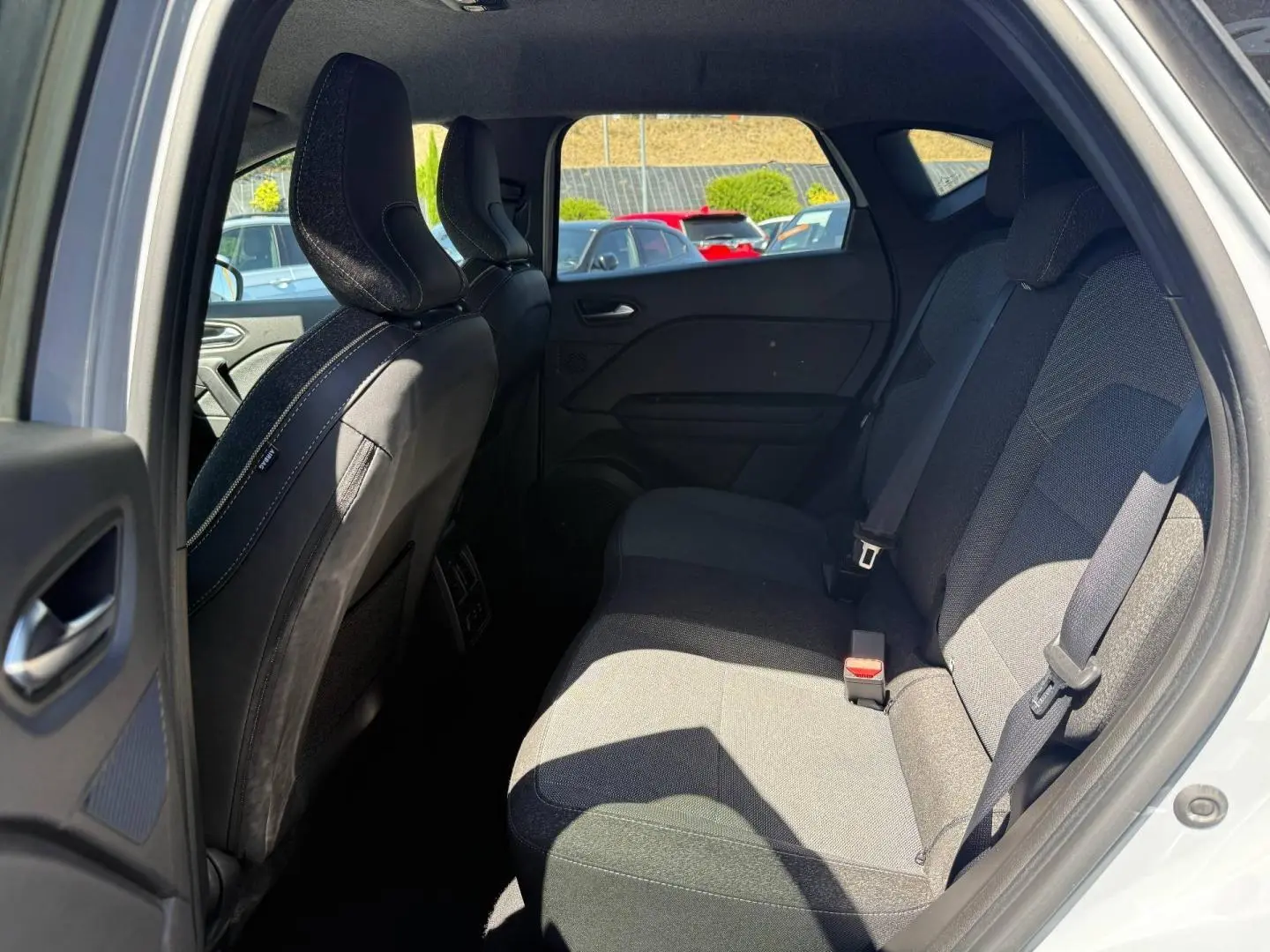 Vue intérieure côté arrière droit du Renault Captur 2025, sièges tissu gris et ceintures visibles.