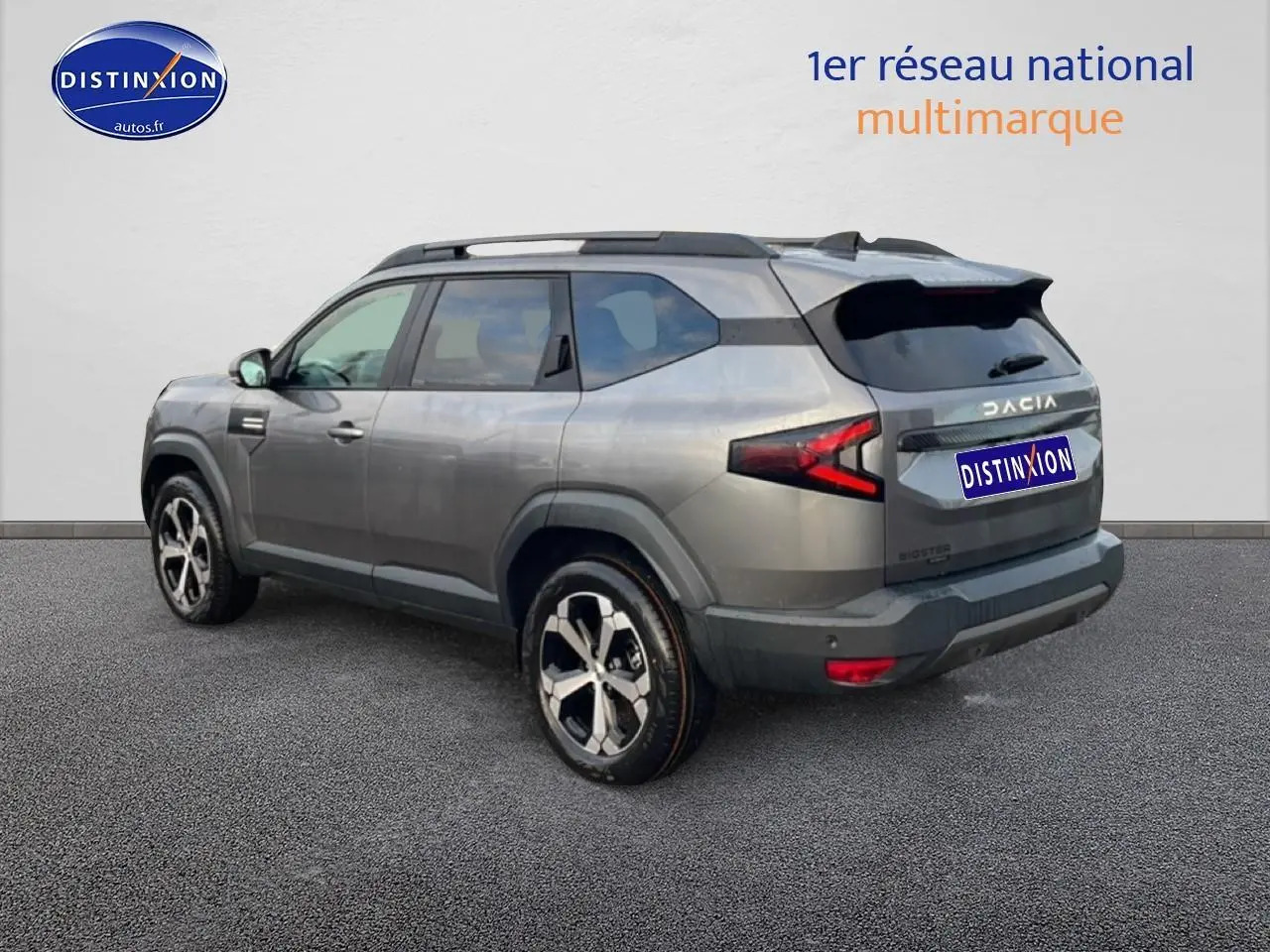 Vue 3/4 arrière droite du Dacia Bigster gris schiste avec jantes alliage diamantées et barres de toit noires.