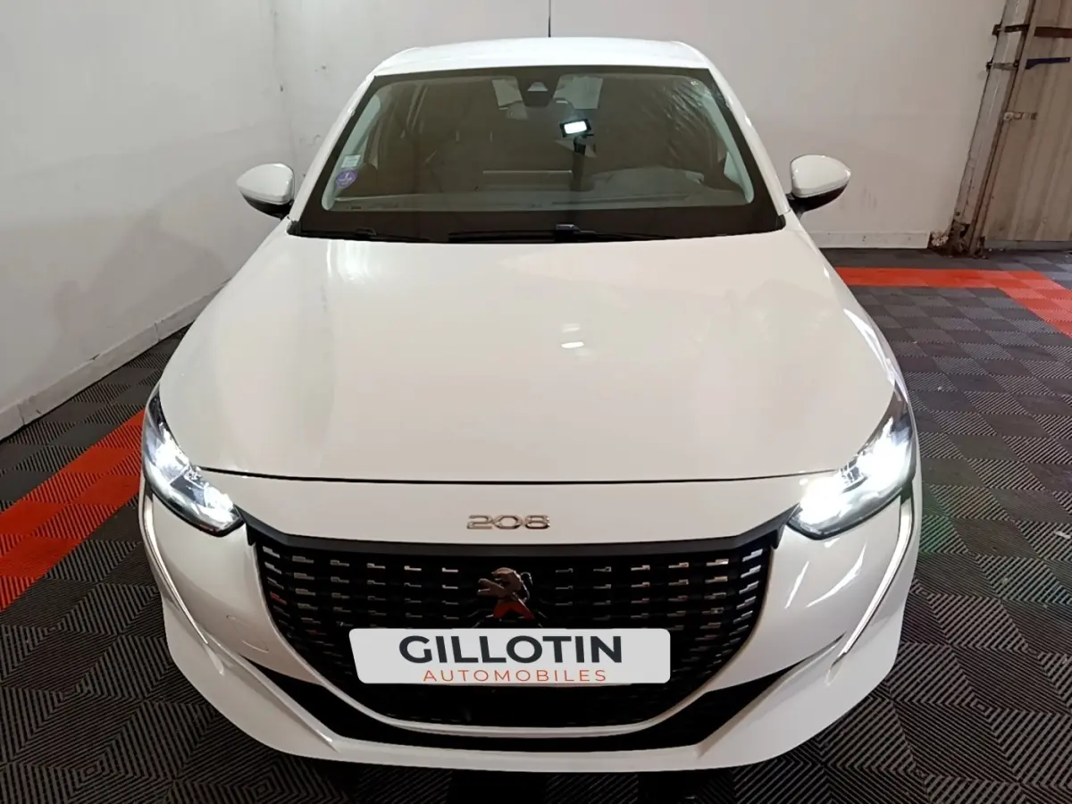 Vue avant d'une Peugeot 208 blanche avec phares LED allumés dans un garage.