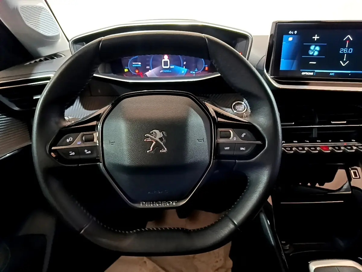 Vue intérieure centrée sur le volant cuir noir de la Peugeot 208 PureTech 100 avec tableau de bord digital et écran tactile.