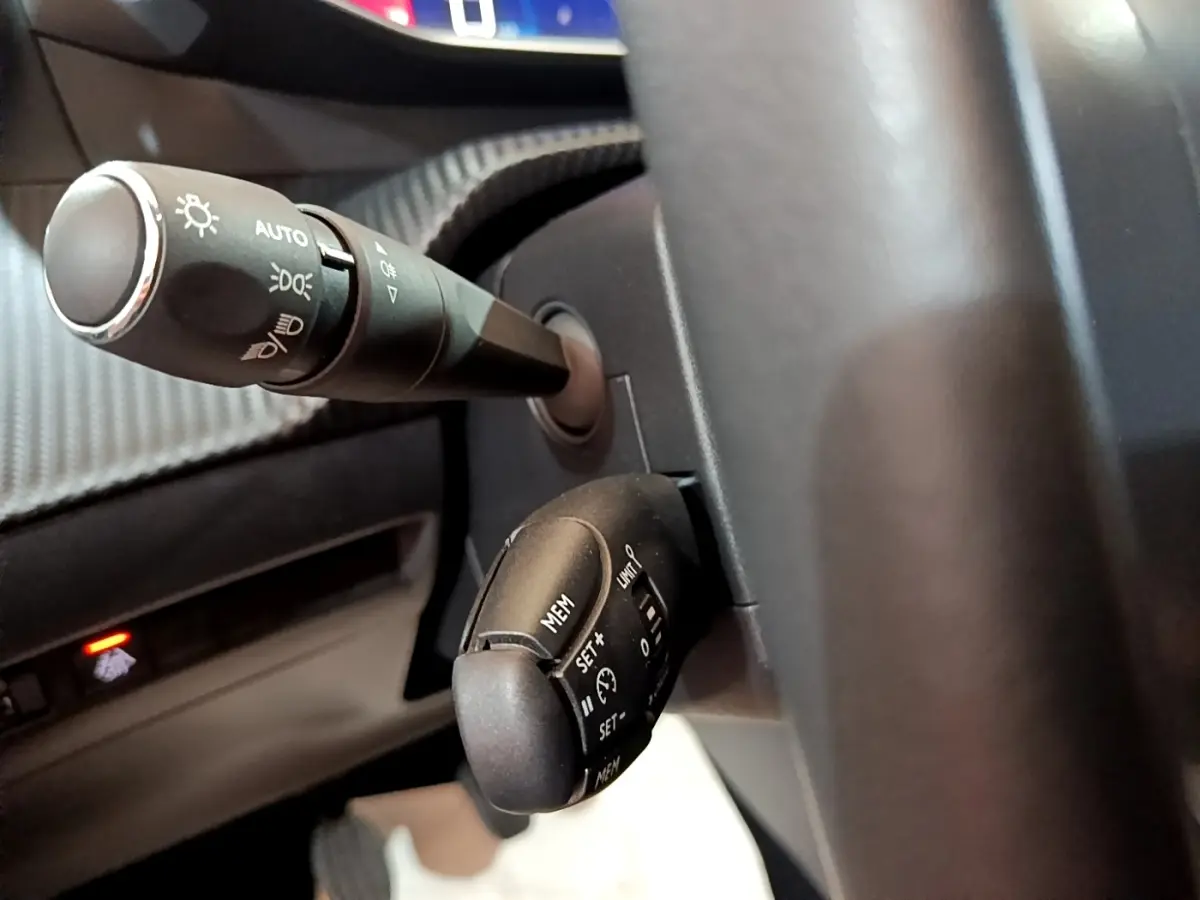 Gros plan sur la commande des phares et régulateur de vitesse du volant d'une Peugeot 208 blanche, vue côté conducteur.