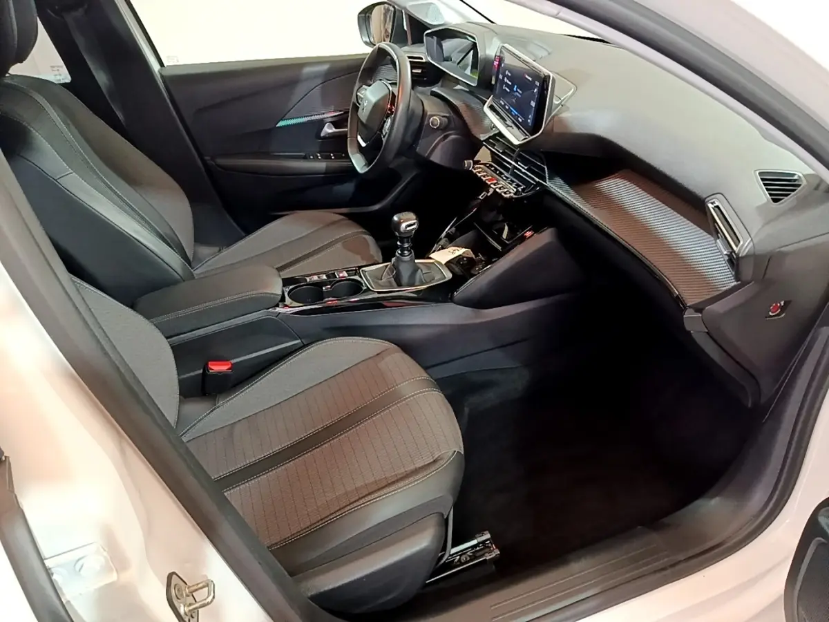 Vue intérieure côté conducteur de la Peugeot 208 blanche, montrant le tableau de bord et la console centrale avec écran tactile.