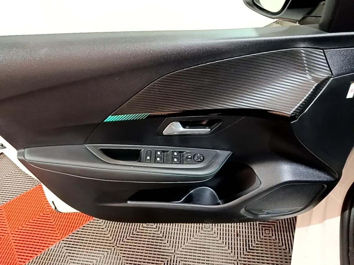 Vue intérieure côté gauche de la porte avant blanche d'une Peugeot 208 avec garniture noire et commandes des vitres.