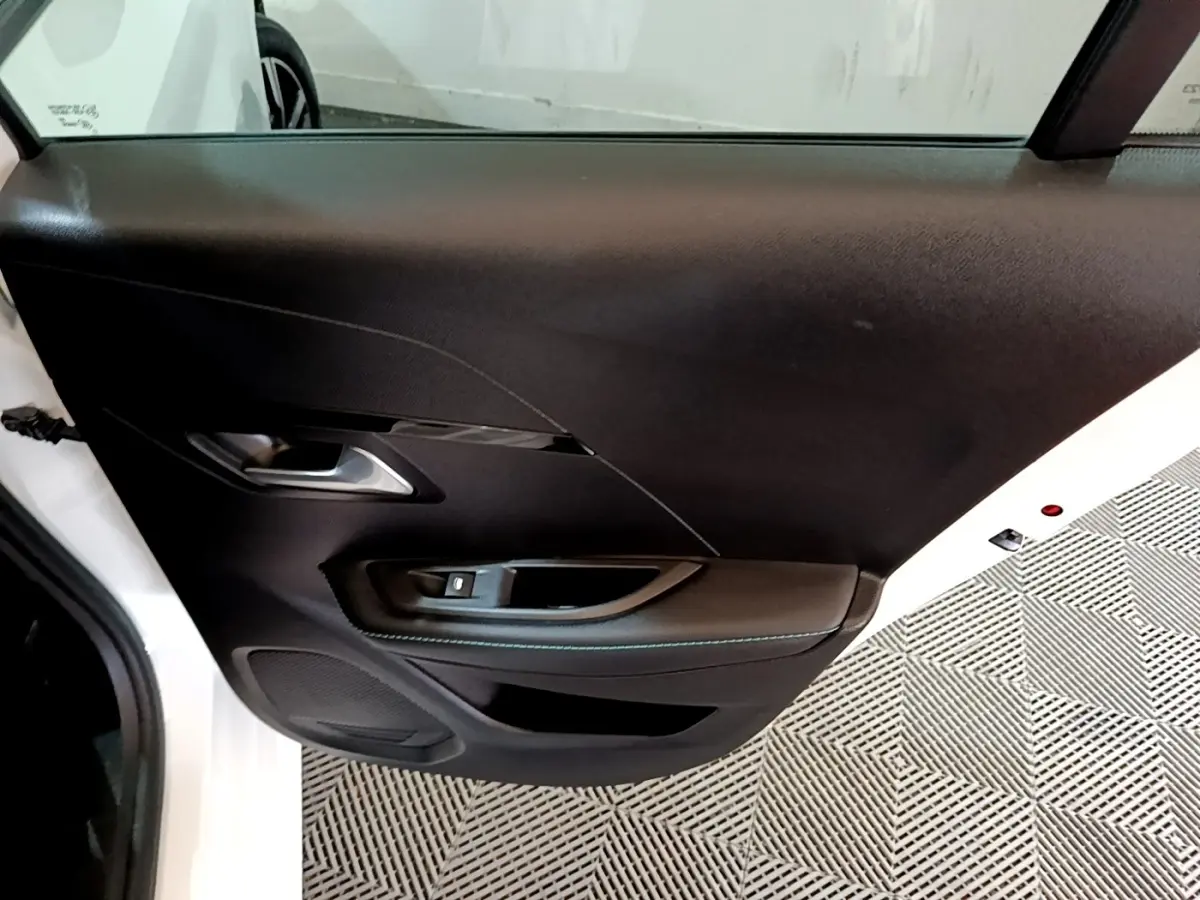Gros plan sur la porte avant gauche noire d'une Peugeot 208 blanche, mettant en valeur la poignée et les commandes de vitre.